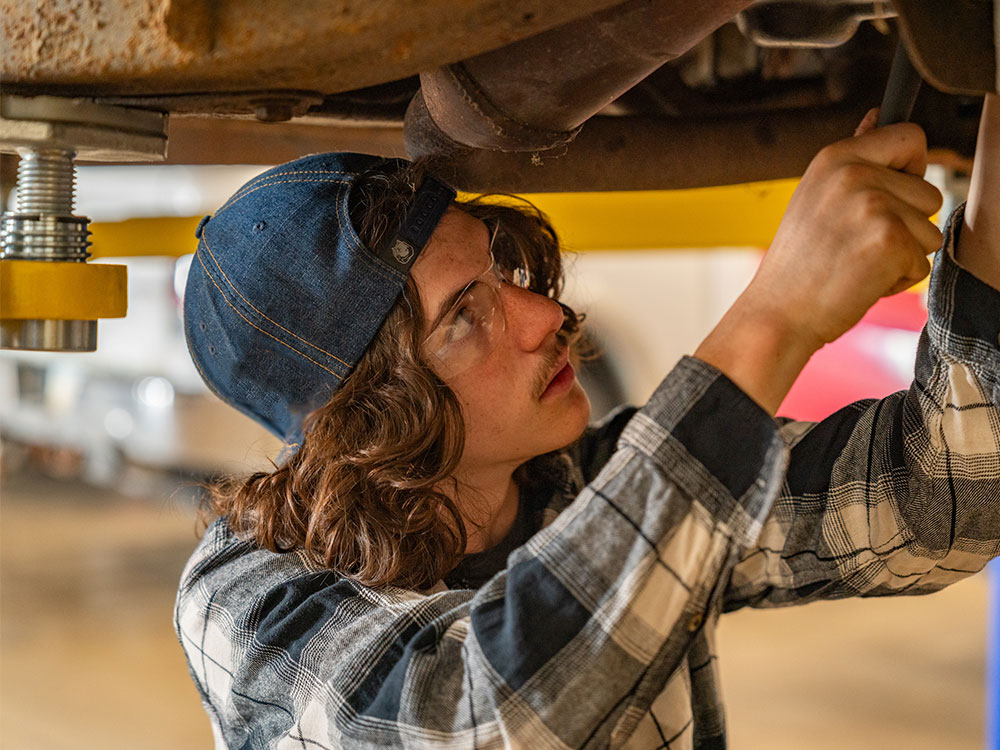Male student working on underside of a car